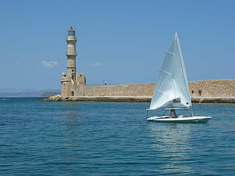 Sailboat passing historic stone lighthouse on sunny summer day