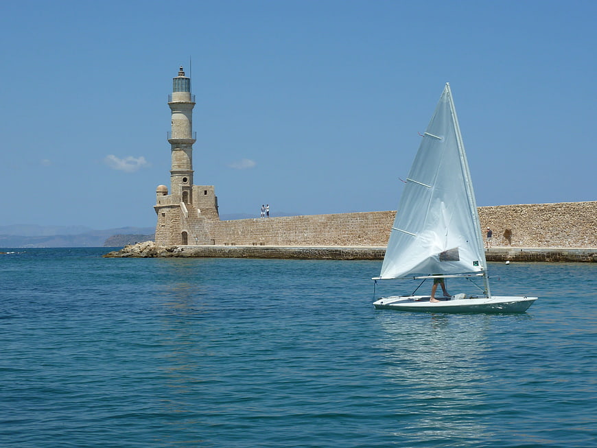 Sailboat passing historic stone lighthouse on sunny summer day