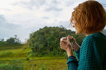 Woman drinking coffee outdoors in a green landscape