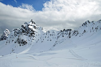 Snow-covered mountain peaks with ski tracks and cloudy sky