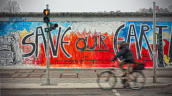 Cyclist passing Save Our Art graffiti on Berlin Wall