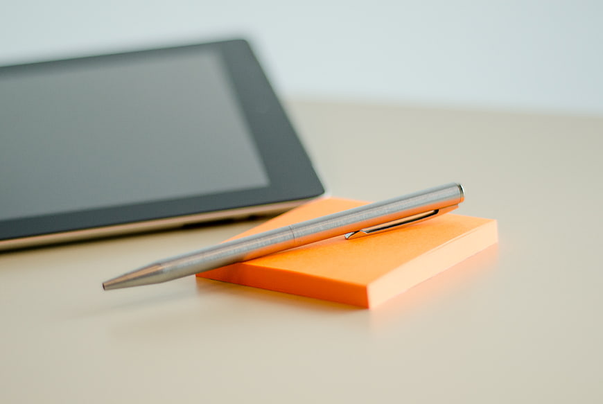 Silver pen on orange sticky notes with tablet background