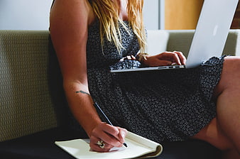 Woman Writing in Notebook with Laptop on Couch