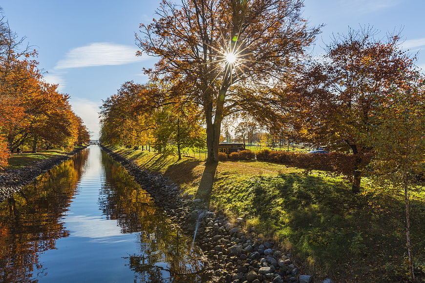 Sunlit Autumn Canal with Vibrant Orange Trees and Reflections