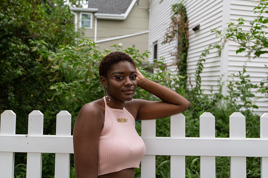 Confident Black Woman in Pink Top by White Fence