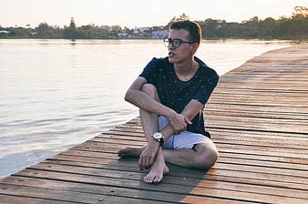 Young man sitting on wooden pier at sunset