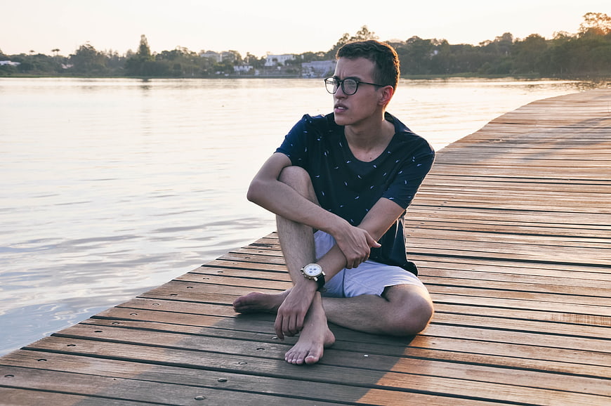 Young man sitting on wooden pier at sunset