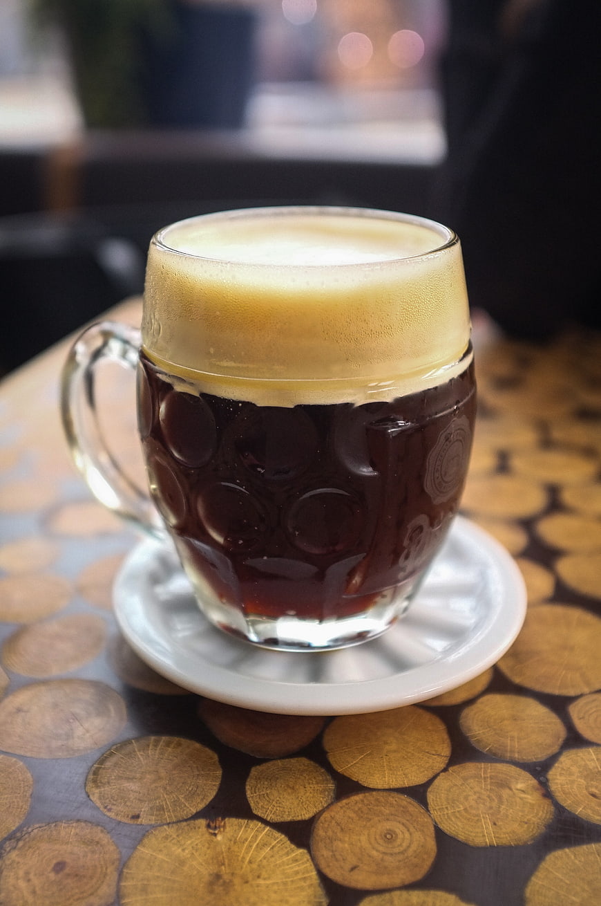 Glass mug of dark beer with foam on wooden table