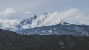 Snowy mountain peaks with clouds and forest landscape