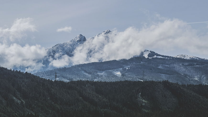 Snowy mountain peaks with clouds and forest landscape