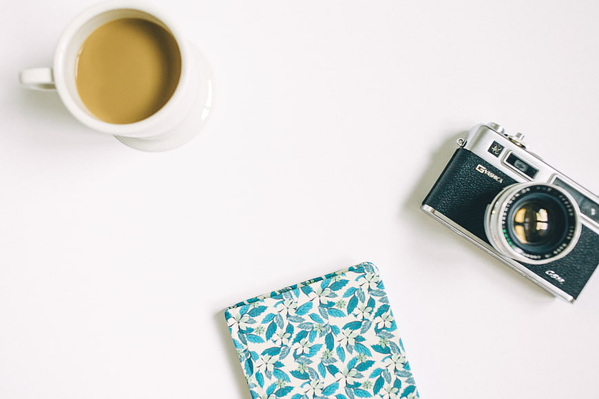 Flat lay of vintage camera, coffee, and floral notebook on white