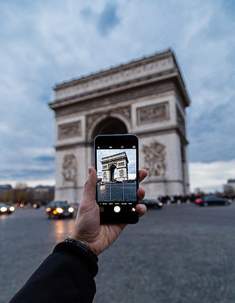Hand holding smartphone photographing Arc de Triomphe in Paris