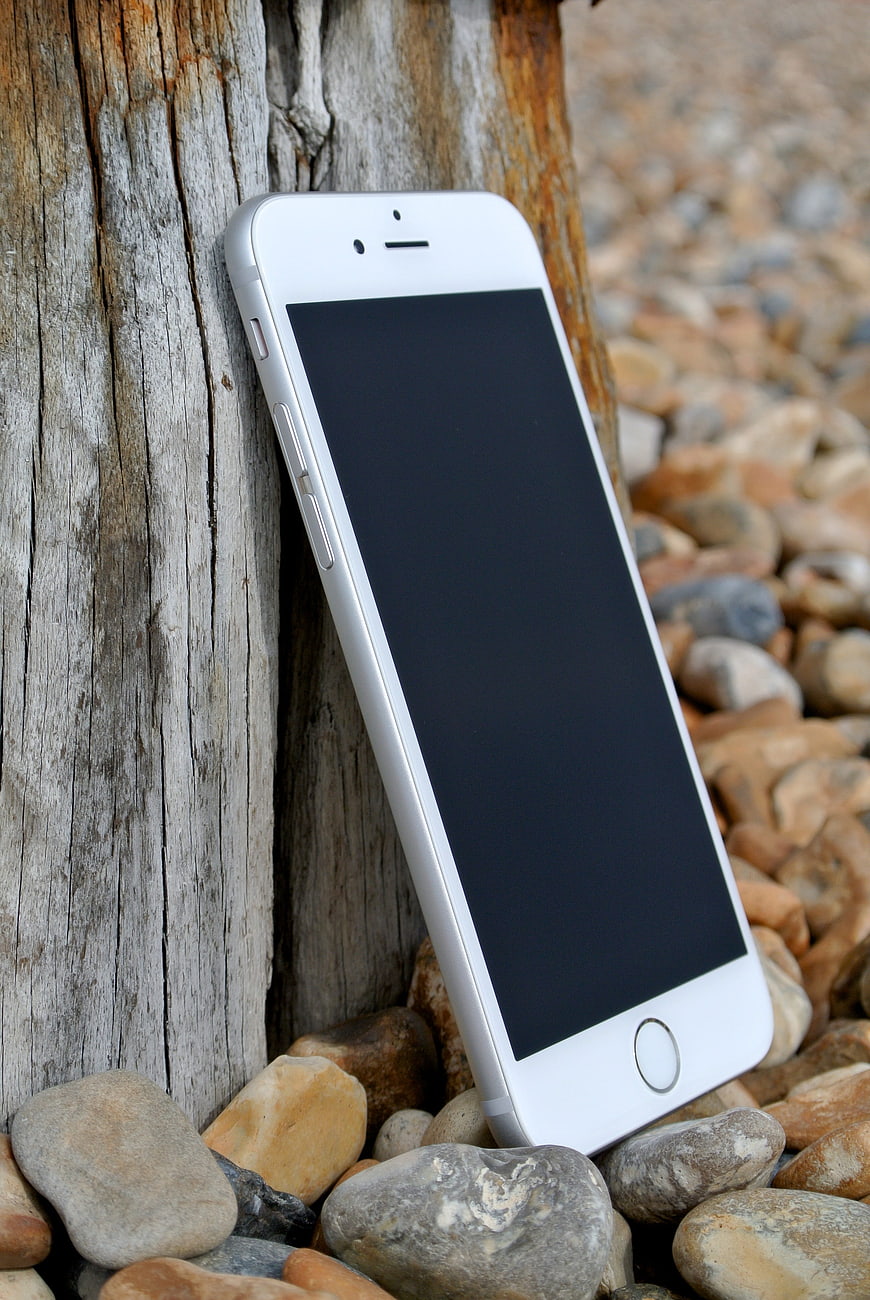 White Smartphone Leaning Against Weathered Wood on Beach