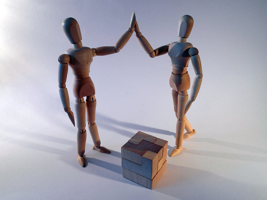Wooden mannequins high-fiving over a wooden puzzle cube