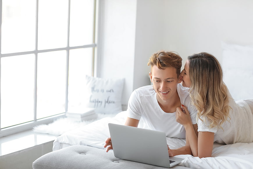 Happy couple using laptop in bright white bedroom