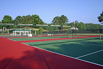 Empty outdoor tennis courts with red and green surfaces under a clear blue sky