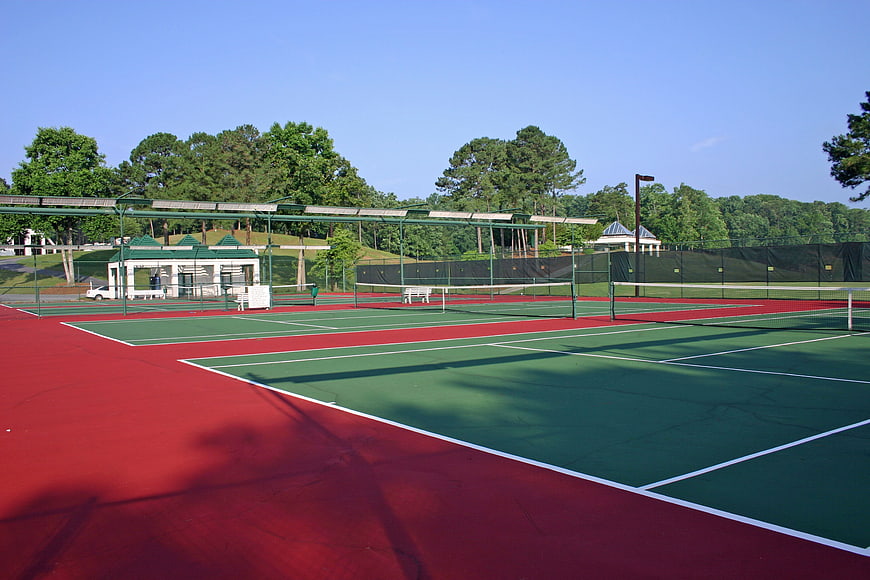 Empty outdoor tennis courts with red and green surfaces under a clear blue sky