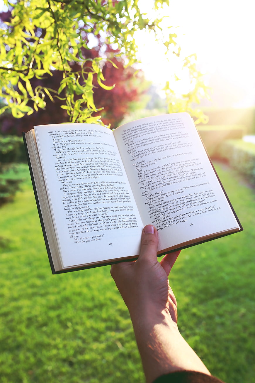 Hand holding open book in sunny garden