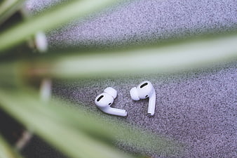 White Wireless Earbuds on Textured Surface with Blurred Plant