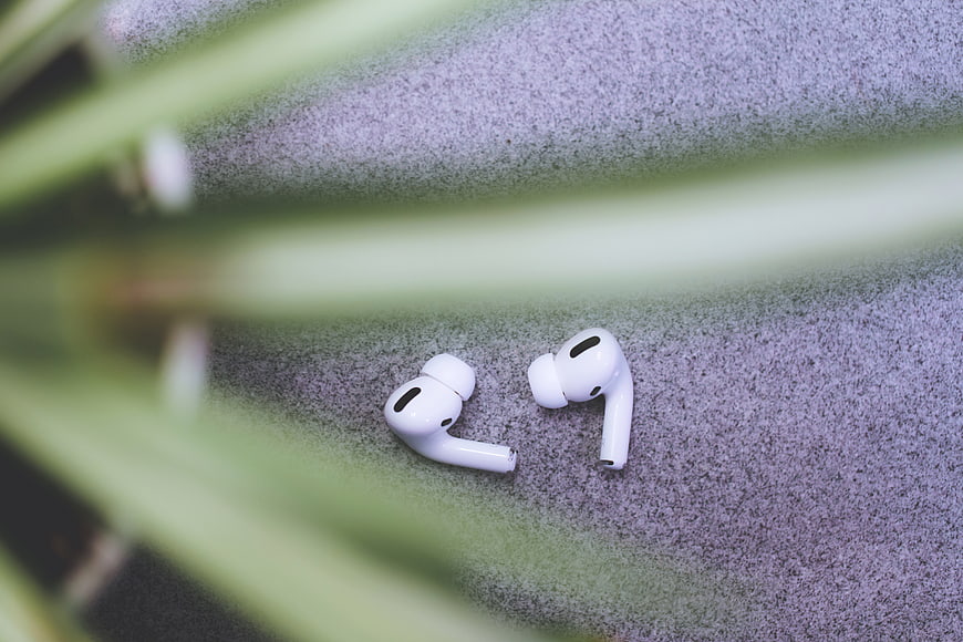 White Wireless Earbuds on Textured Surface with Blurred Plant