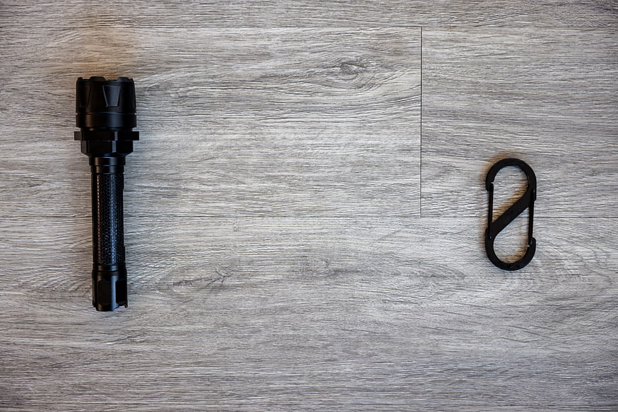 Black flashlight and carabiner on gray wood background