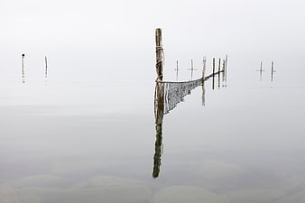 Minimalist wooden posts and net in foggy calm water