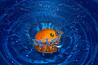 Orange splashing into blue water with dynamic droplets