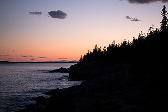 Silhouetted Rocky Coastline at Sunset Over Calm Ocean