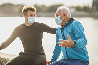 Senior and young man wearing masks talking outdoors