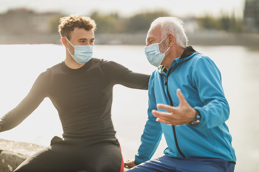 Senior and young man wearing masks talking outdoors
