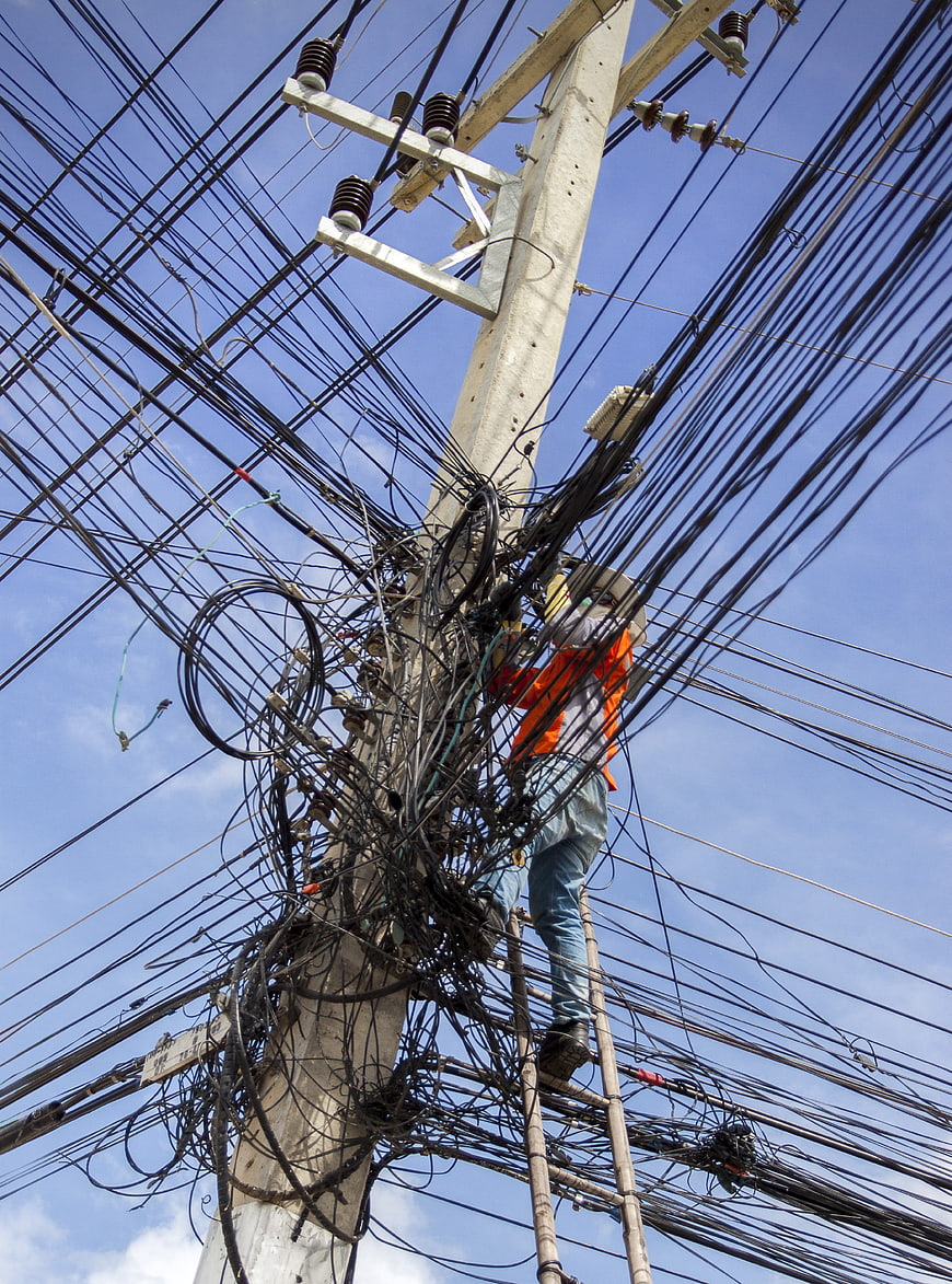Electrician climbing utility pole tangled with chaotic wires