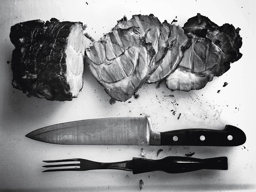 Sliced roast beef with knife and fork on cutting board