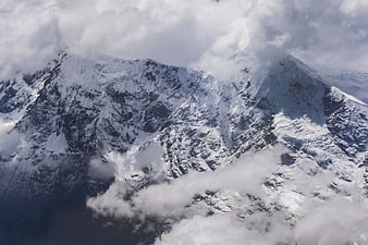 Aerial view of snow-covered mountain peaks through clouds