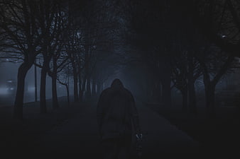 Silhouette of hooded figure walking down foggy dark road