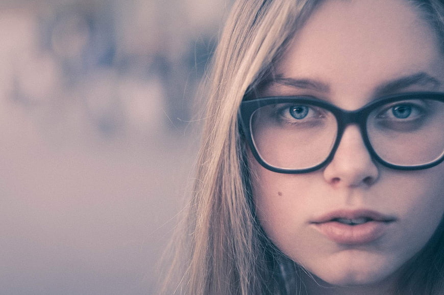 Close-up portrait of blonde woman with glasses looking at camera