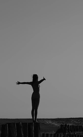 Silhouette of Woman Standing on Wooden Post with Arms Outstretched