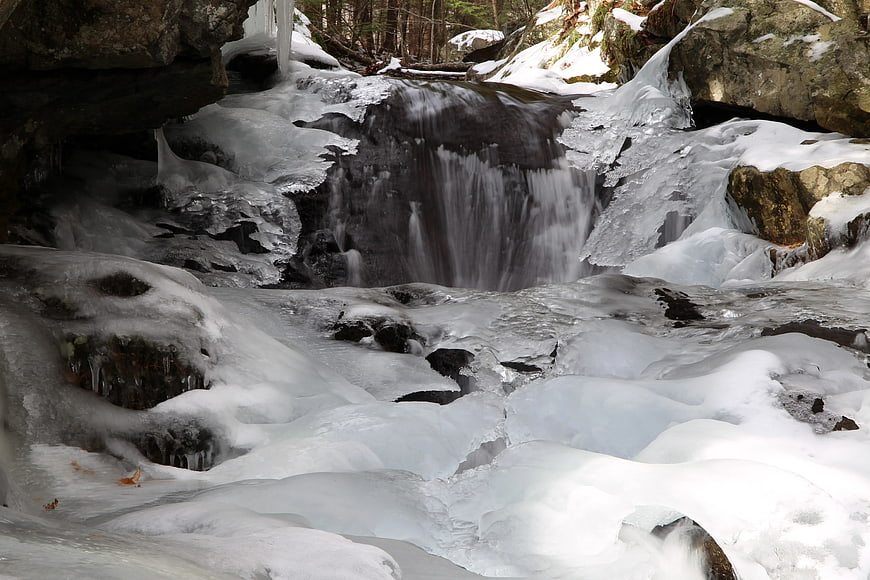 Frozen waterfall in winter forest with flowing water