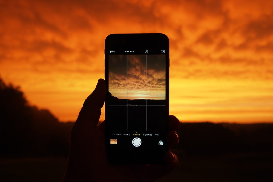 Hand holding smartphone capturing vibrant orange sunset landscape