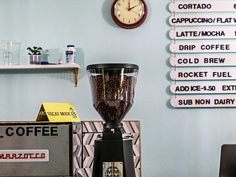 Coffee grinder with beans and menu board in cafe