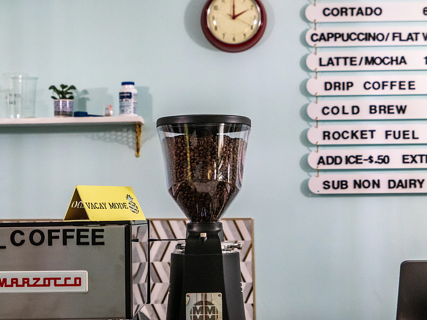 Coffee grinder with beans and menu board in cafe