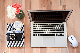 Flat lay workspace with laptop, camera, and flowers on wooden desk