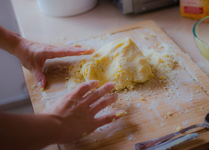 Hands kneading yellow dough on wooden board