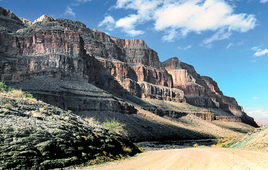 Dirt road winding through red rock canyon cliffs under blue sky