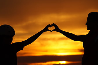 Silhouette of mother and child making heart shape at sunset