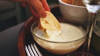 Hand Dipping Bread into Garlic Aioli Sauce in Glass Bowl
