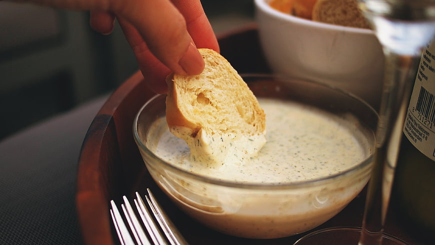 Hand Dipping Bread into Garlic Aioli Sauce in Glass Bowl