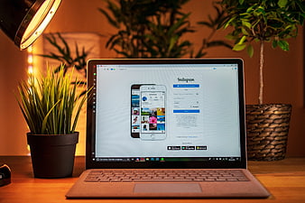 Laptop displaying Instagram interface on a wooden desk with potted plants