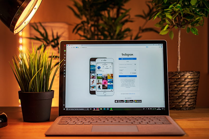 Laptop displaying Instagram interface on a wooden desk with potted plants