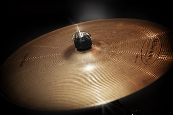 Close-up of a golden brass drum cymbal on black background