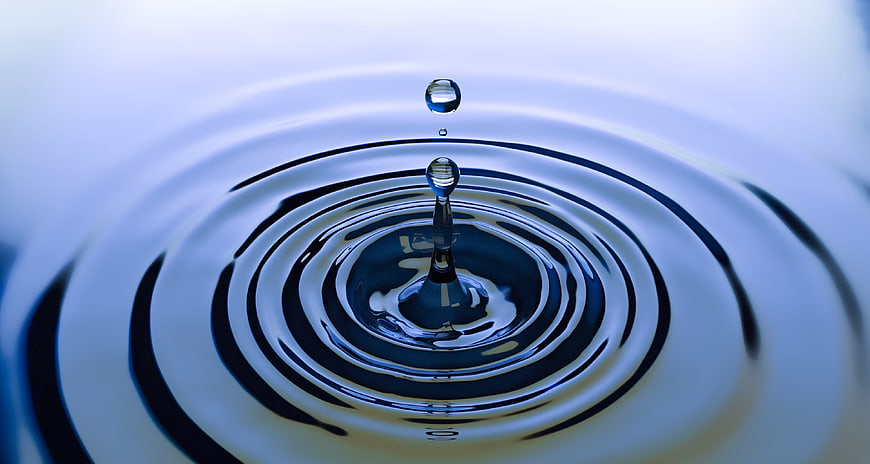 Macro water drop splash with ripples on blue surface